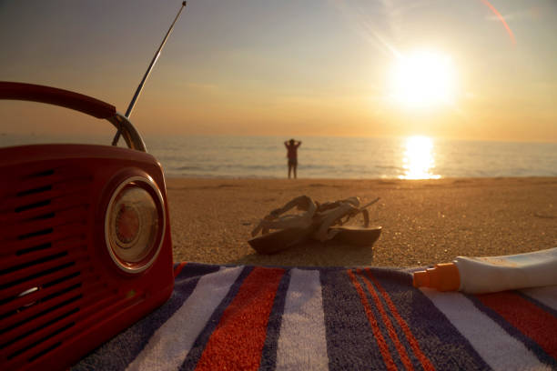 ver más allá de la radio, libro y sandalias a la mujer en la playa - moody sky audio fotografías e imágenes de stock