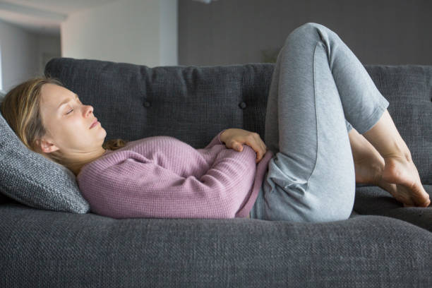 istock Sick woman lying on back on grey sofa, holding hands on stomach 1131278569