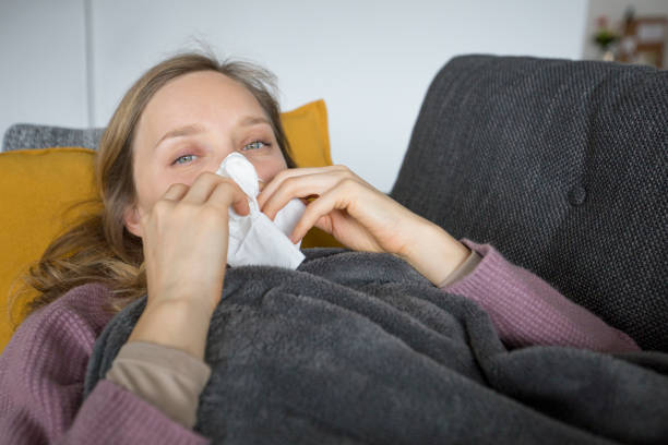 istock Sick woman lying on sofa at home, blowing her nose with napkin 1131278574