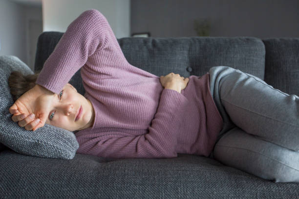 istock Sick woman lying on sofa, holding hands on stomach and head 1131278578