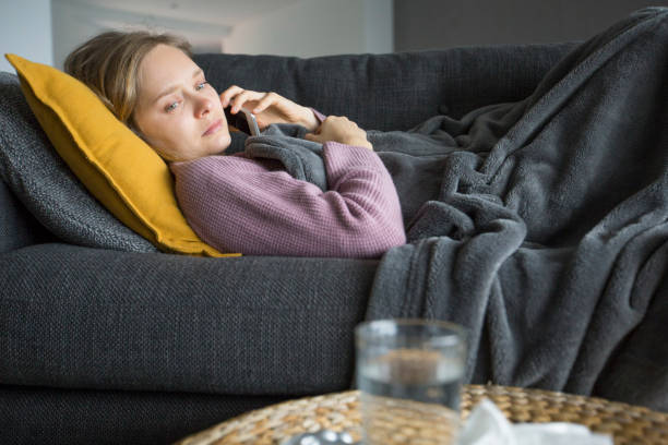 istock Sick woman lying on sofa at home, calling husband on phone 1131278591