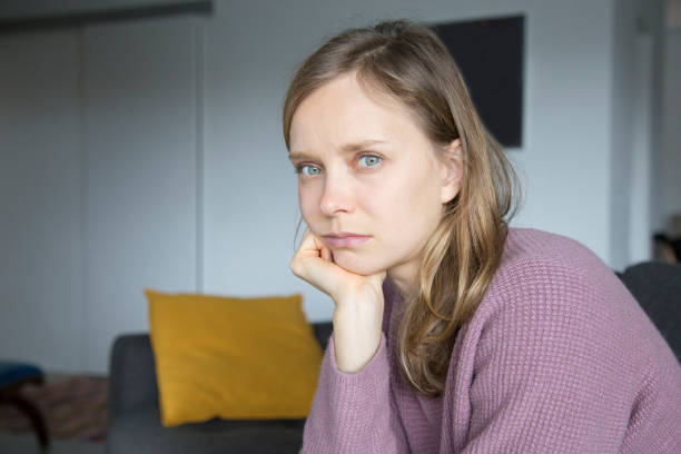 istock Upset young woman sitting on sofa at home, looking at camera 1131278626