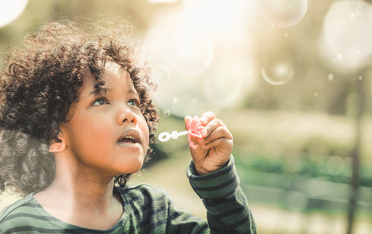 Happy little kid blowing soap bubble in school garden. Child outdoor activity concept.