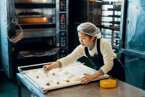 Mid adult woman baking bread in an industrial kitchen Mid adult woman baking bread in an industrial kitchen in Japan baker occupation stock pictures, royalty-free photos & images