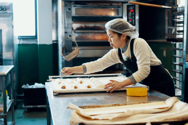 ミッドアダルト女性は、工業用キッチンでパンを焼く - パン職人　日本 ストックフォトと画像