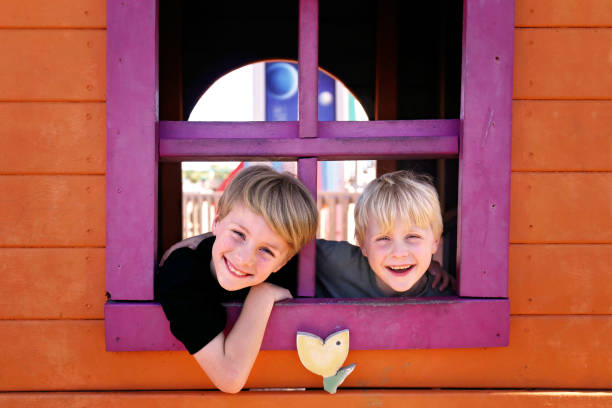 Happy Little Kids Smiling at the Park as they Peek out the Window of a Clubhouse Fort Two happy little kids, brothers, are smiling at the park as they peek out the window of a clubhouse fort. collorful stock pictures, royalty-free photos & images