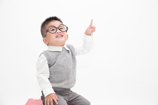 Portrait of Asian baby boy with finger pointed up. Cute little boy wearing white shirt, grey vest and glasses isolated on white background. Creative ideas and innovation technology education concept