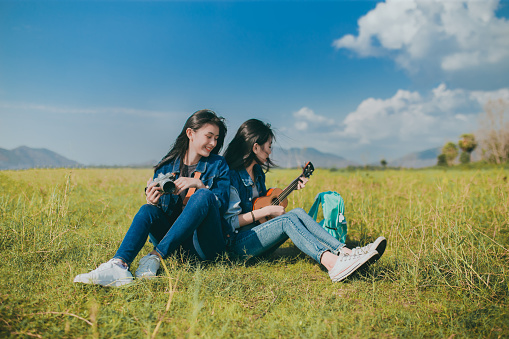 Friendship of Asian teenager women resting outdoor with camera and ukulele her playing music relax.