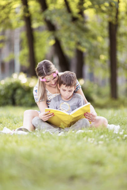 istock Mother and son sitting on a grass in park and reading a book 1131301619