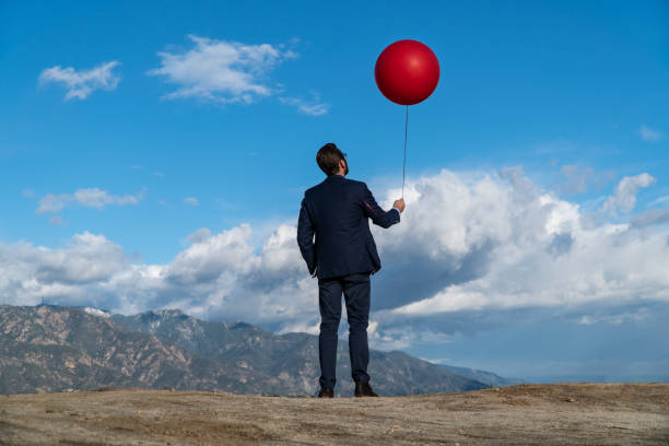 istock Businessman Holding Red Balloon Against Blue Cloudy Sky 1131301749