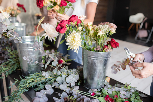 Close-up flowers in a metal bucket. Florist workplace. Woman arranging a bouquet with roses, chrysanthemum, carnation and other flowers. A teacher of floristry in master classes or courses