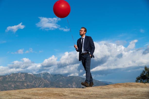 istock Businessman Holding Red Balloon Against Blue Cloudy Sky 1131303843