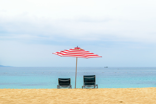 Empty beach chairs under large red and white striped patio umbrella on a beautiful tropical Caribbean white sand beach
