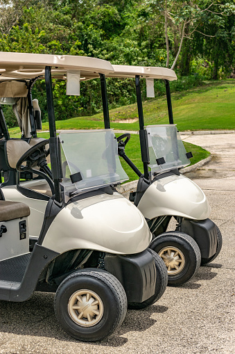 Two empty white golf carts parked side by side on the driveway of golf course