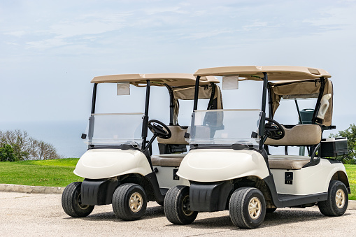 Two empty white golf carts parked side by side on the driveway of golf course