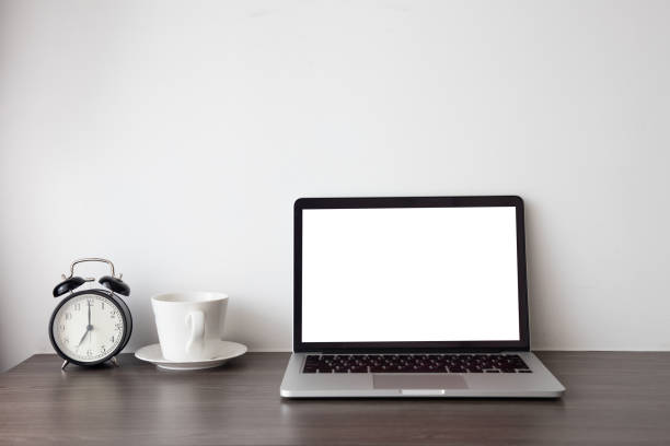 istock wood office table with blank screen on laptop, notebook and hot coffee cup, retro black clock on white cement background. 1131311286