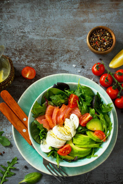 istock Diet menu concept. Summer Healthy salad with Tomatoes, Salmon, Egg, Avocado and arugula on a dark stone table. Top view flat lay background. Copy space. 1131316897