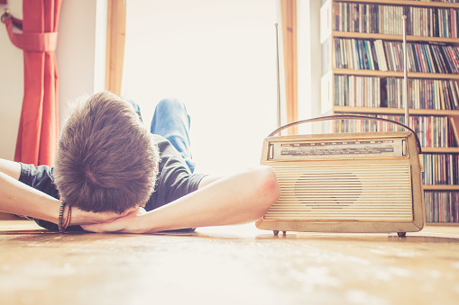 Young man lying on the floor is listening to a vintage radio, free time