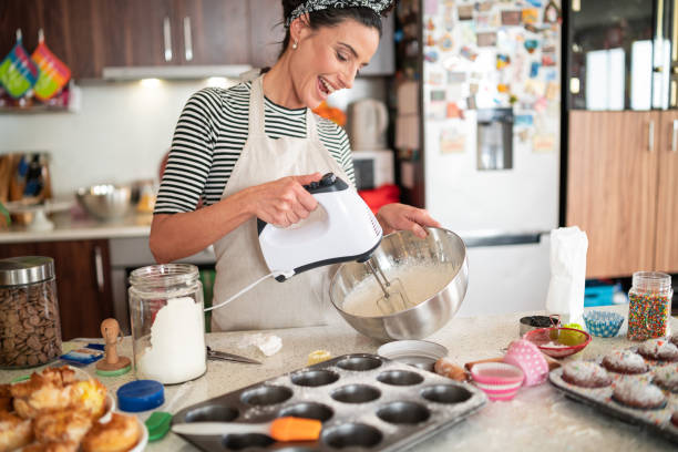 femme de confiserie faisant la crème délicieuse pour des cupcakes - batteur électrique photos et images de collection