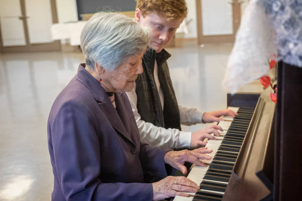 muzykoterapia, starsza azjatka grająca na fortepianie z młodym mężczyzną - muzykoterapia zdjęcia i obrazy z banku zdjęć