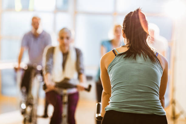 vista posteriore dell'istruttore di spin bike durante la lezione di ginnastica in palestra. - spinning instructor exercising gym foto e immagini stock