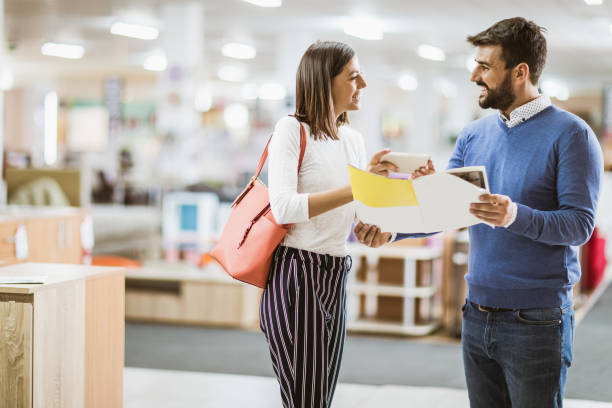 istock Happy couple using mobile phone while reading catalog in furniture store. 1131335504