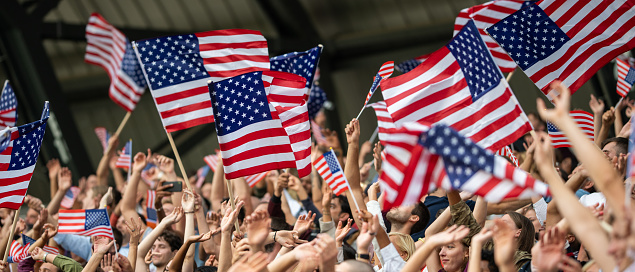 Fans holding US Flags and cheering while watching match in stadium.