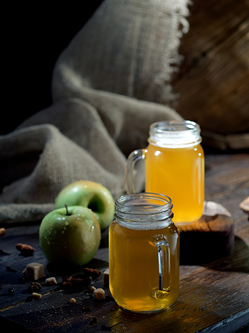 Apple cider served in mason jars on the table with fresh apples, spices and a cask on the background