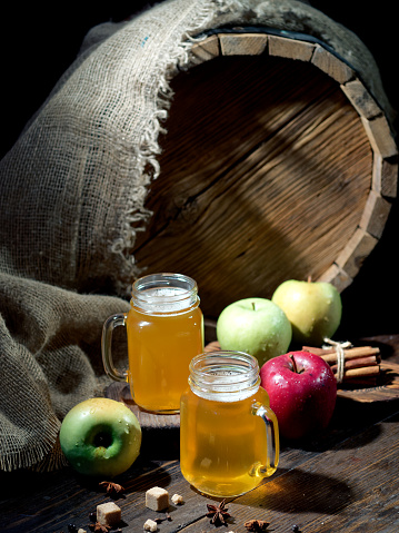 Apple cider served in mason jars on the table with fresh apples, spices and a cask on the background