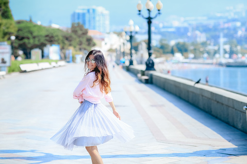 Girl walking along the seafront in dress in hot summer day.