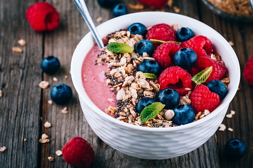 Acai smoothie and granola bowl with fresh raspberries and blueberries on wooden background