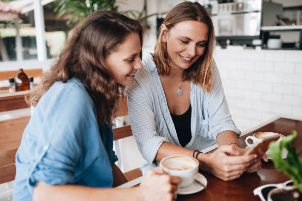 istock Two beautiful happy women looking in smartphone in cafe. 1131347089
