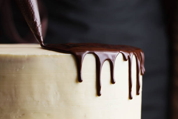 The process of decorating the cake with liquid chocolate. A confectioner squeezes liquid chocolate from a pastry bag on to a white cream biscuit cake. The concept of homemade pastry, cooking cakes.