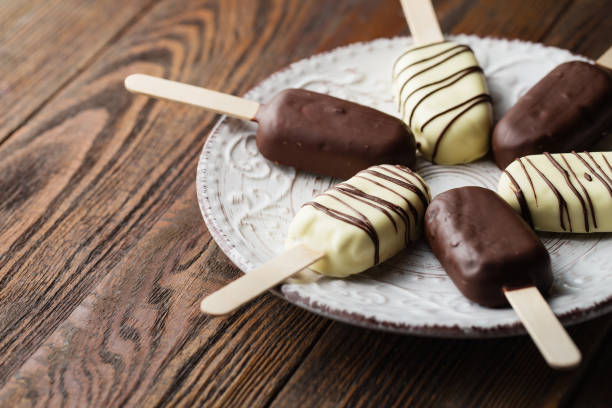 istock Milk chocolate popsicles on a stick. Ice cream popsicles covered with white and dark chocolate on the plate on wooden background. Space for text 1131347113