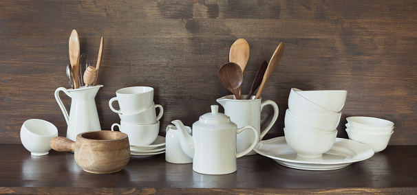 Crockery, porcelain, white utensils and other different stuff on wooden countertop. Kitchen still life as background for design.