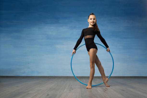 A girl gymnast in a black bathing suit looks in profile in the hands of a gymnastic hoop A girl gymnast in a black bathing suit looks in profile in the hands of a gymnastic hoop. On a blue background rhythm photos stock pictures, royalty-free photos & images