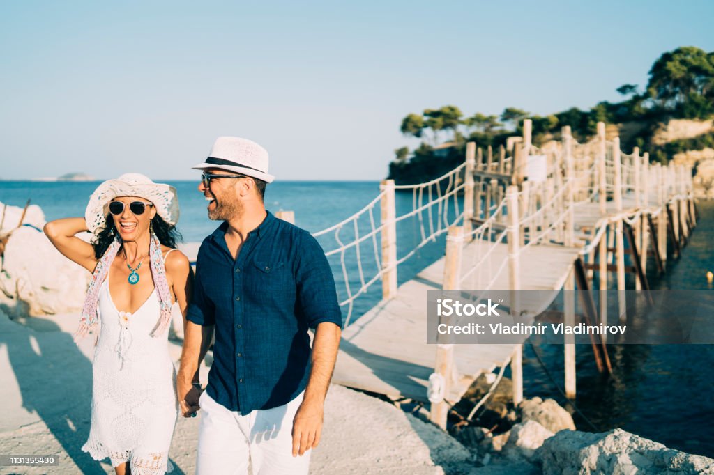 Cheerful couple walking  and holding hands Cheerful couple walking  and holding hands in front of Cameo island in Zakynthos Adult Stock Photo