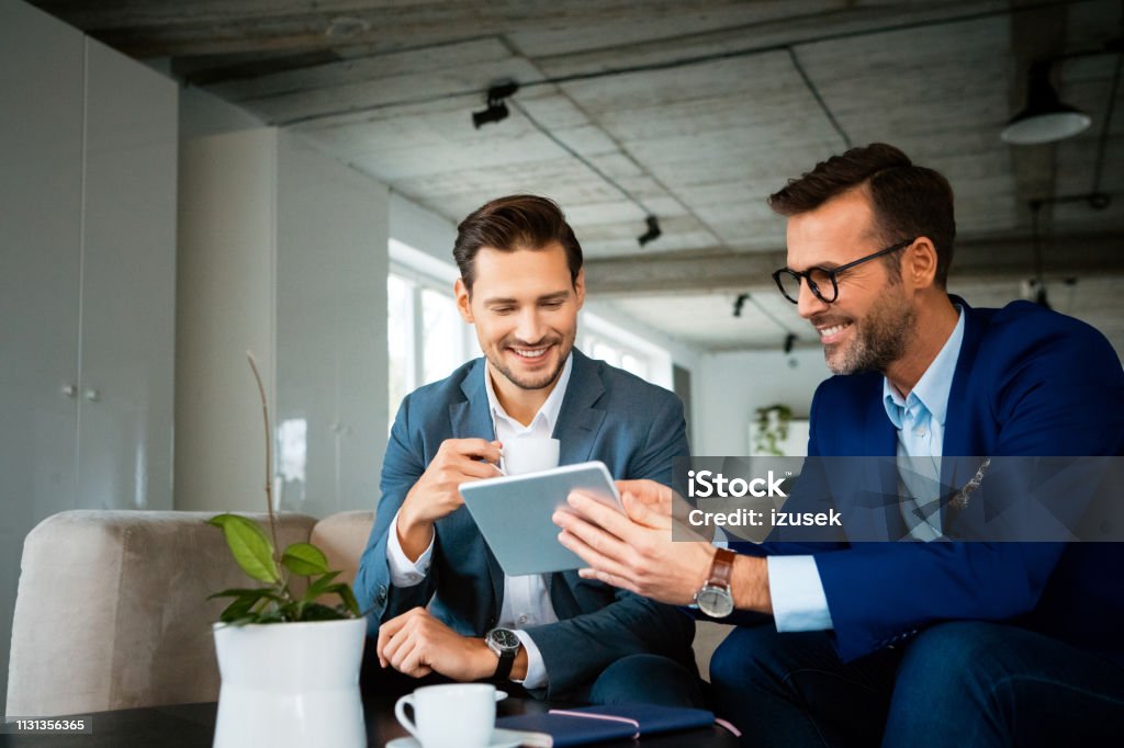 Smiling colleagues discussing over digital tablet Smiling male professionals discussing over digital tablet. Confident colleagues are planning strategy during meeting. They are working at creative office. 30-39 Years Stock Photo