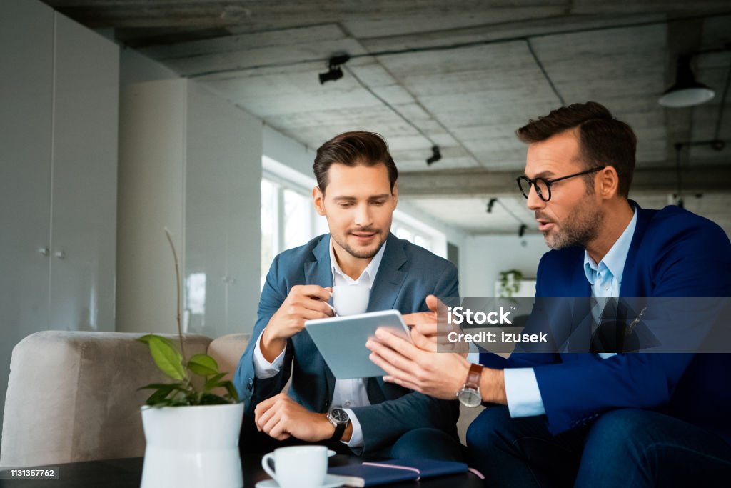 Male professionals discussing over digital tablet Confident male professionals discussing over digital tablet. Colleagues are planning strategy during meeting. They are working at creative office. Business Person Stock Photo