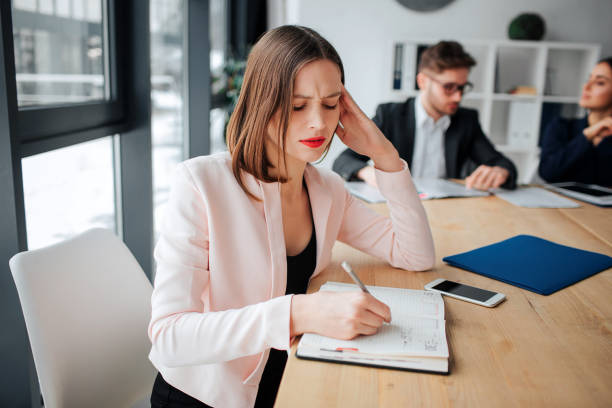 istock Busy thoughtful young woman sit at table in room and writing in notebook. Her colleagues work behind. She is concentrated. 1131357808