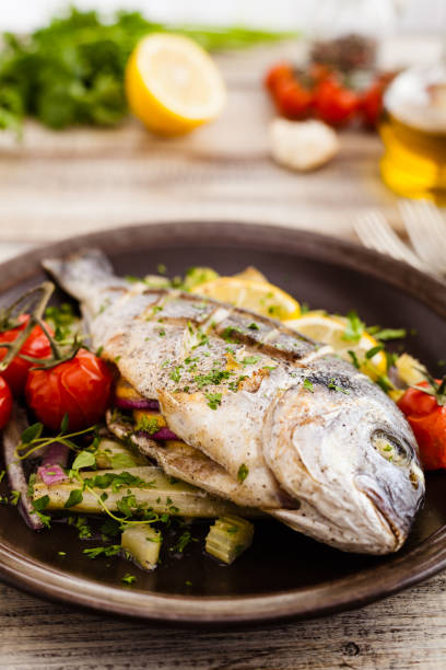 istock Baked whole fish, served with roasted vegetables and lemon. 1131358313