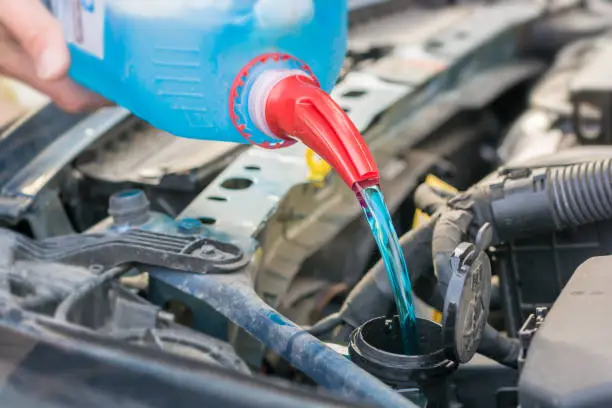Photo of Filling the water tank with antifreeze in the engine compartment of a car