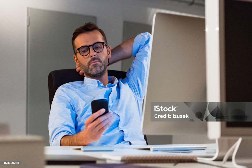 Mature businessman using smart phone at office Mature businessman using smart phone at creative workplace. Male professional is working late at office. He is sitting at desk. 40-44 Years Stock Photo