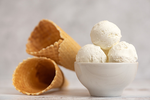 Bowl of vanilla ice cream and waffle cones on light background. Side view.