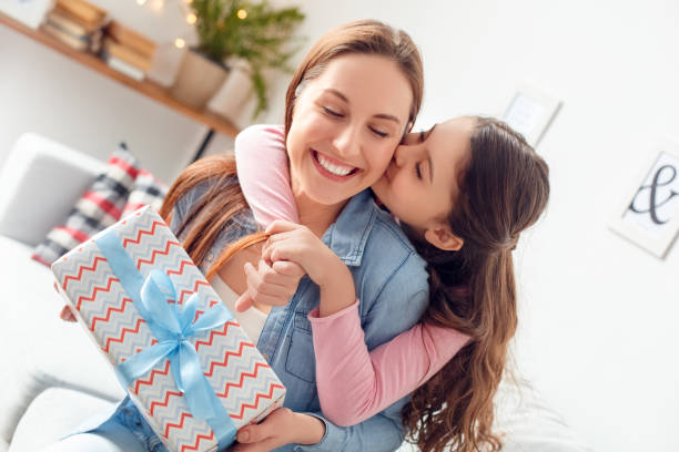 Mother and daughter at home mother's day sitting daughter hugging mom holding present kissing Young woman and girl at home celebrating mother's day sitting on sofa daughter hugging mom holding present box kissing cheek closed eyes pleasure close-up. cute pregnant woman with gift stock pictures, royalty-free photos & images