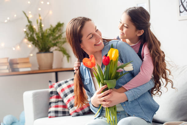 Mother and daughter at home mother's day daughter hugging mother with bouquet of flowers happy Young woman and girl at home celebrating mother's day sitting daughter hugging mother holding bouquet of flowers looking at each other smiling happy cute pregnant woman with gift stock pictures, royalty-free photos & images