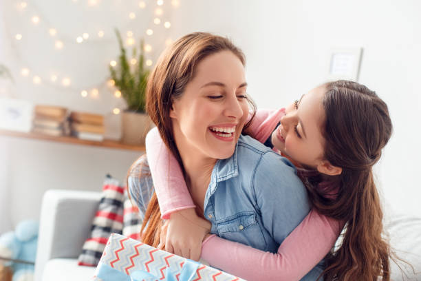 Mother and daughter at home mother's day sitting daughter hugging laughing mom close-up Young woman and girl at home celebrating mother's day sitting on sofa daughter hugging mom laughing cheerful holding present box close-up cute pregnant woman with gift stock pictures, royalty-free photos & images