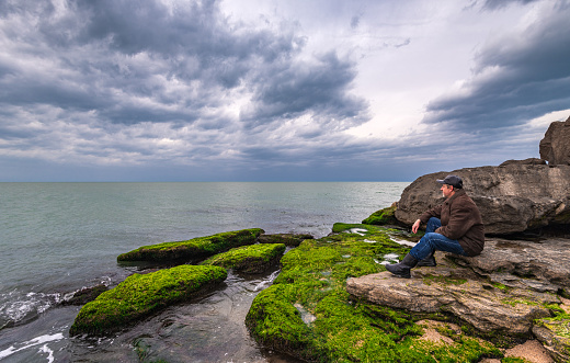 Traveler on a rocky seashore overgrown with green algae