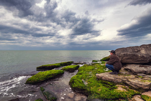 Traveler on a rocky seashore overgrown with green algae