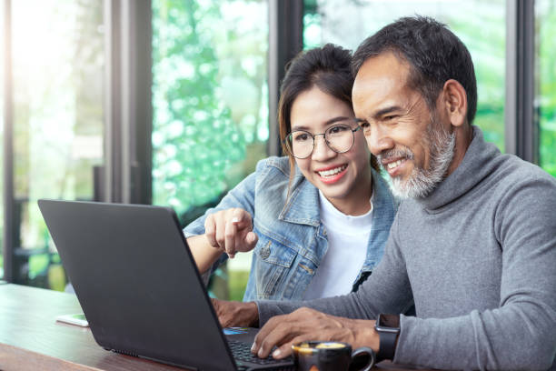 homme asiatique mûr attrayant avec la barbe courte élégante blanche regardant l'ordinateur portable avec la femme de hipster de lunettes d'oeil d'adolescent dans le café. enseigner l'internet en ligne ou la technologie wifi dans le concept d'homme plus - caucasian male female offspring photos et images de collection